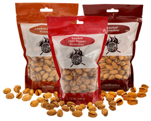 Three packages of smoked chili pepper pistachios with pistachios scattered around on a black background.