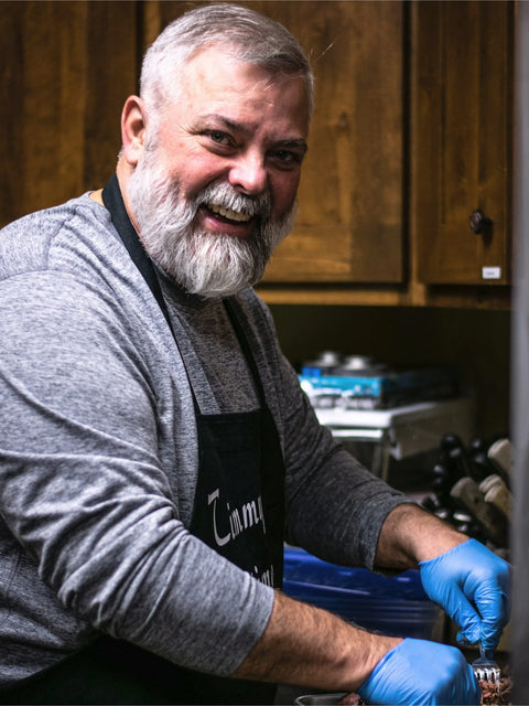 Man in a kitchen wearing an apron and gloves, likely preparing food.