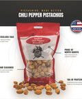 A 12 oz resealable bag of Smoked Chili Pepper Pistachios by The Pine Ridge Creamery, shown on a white and black graphic background with callout text highlighting features like resealable bag, hand seasoned, and pride of North Dakota. Several whole pistachios are scattered in front of the bag.