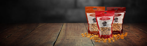 Three bags of Timmy's Pastime Pistachios arranged on a rustic wooden tabletop against a dark, blurred background.