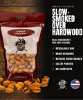A bag of Smoke Paste Smoked Pistachios displayed on a dark wood background with scattered whole and cracked pistachios in front. The packaging is red, white, and clear, showing the pistachios inside.